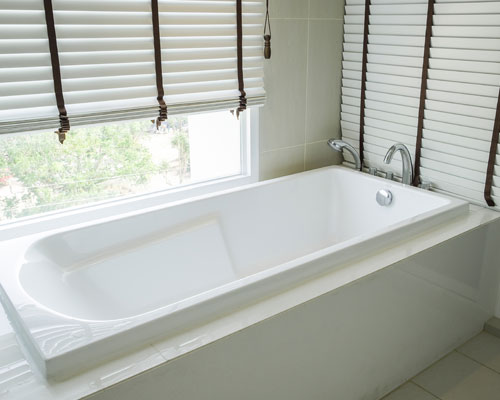 White jetted bathtub with tan tile surround installed beneath a window