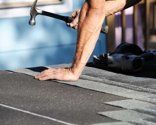 Roofer installing asphalt shingles with hammer on residential roof